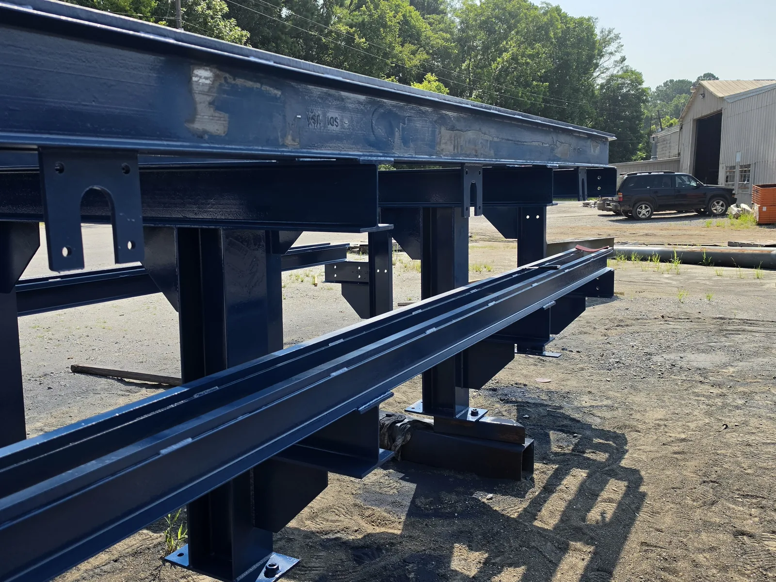 Painted steel crane runway beams with welded seats and stiffeners on stands in a fabrication yard